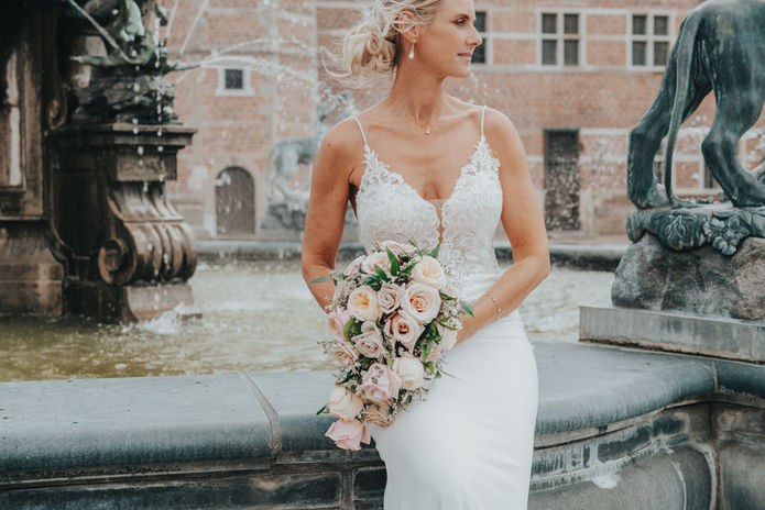 Bride in lace gown holds a rose bouquet by a historic fountain at a Cyprus wedding
