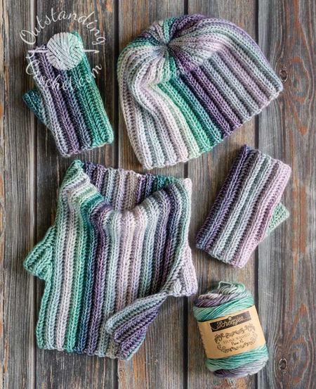 A flat lay of Ryft unisex crochet set: a striped ribbed hat, a matching cowl neck warmer, and fingerless gloves. The multicolored yarn creates a seamless transition between vertical stripes, highlighting the thick, vertical ribbing texture of the Aran weight cotton yarn in green and purple shades.