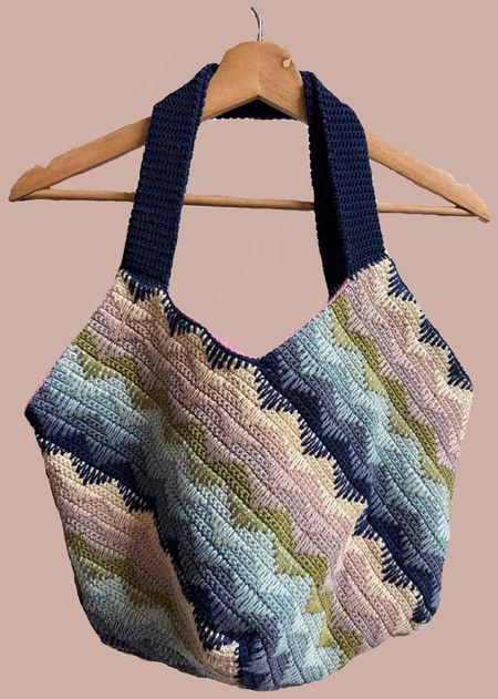 Handmade slouchy crochet shoulder bag featuring vibrant diagonal stripes in a multi-colored spike stitch pattern. The bag is shown in a relaxed, stylish drape, highlighting its large capacity.