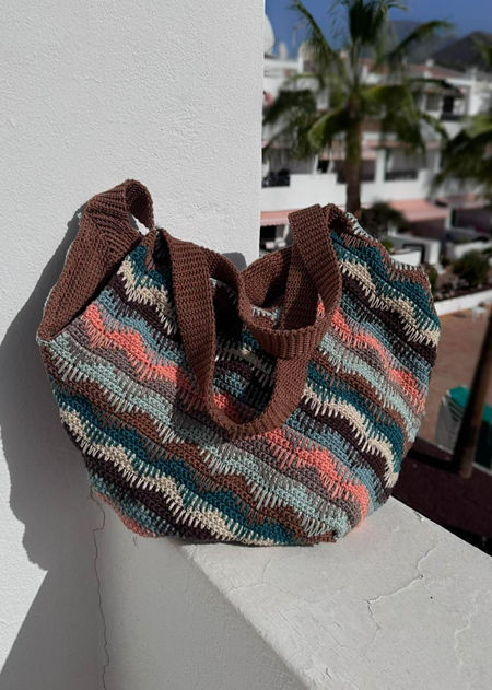 Handmade slouchy crochet shoulder bag featuring vibrant diagonal stripes in a multi-colored spike stitch pattern. The bag is shown in a relaxed, stylish drape, highlighting its large capacity.