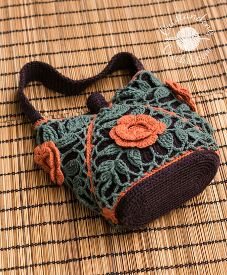 Small crochet purse composed of 4 joined-as-you-go triangular motifs. The design features sage green leaf lace patterns over a dark brown lining, trimmed with bright orange diagonal seams and a matching 3D crochet flower on the front. Measures 20 cm wide by 17 cm high with a dark brown oval base and a handle.