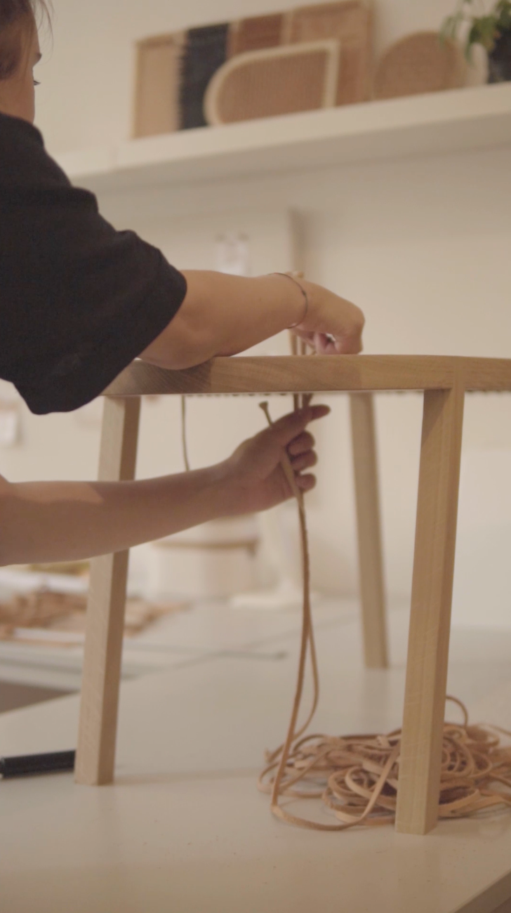 Mains tissants des lanières de cuir à un banc, illustrant une étape clé dans la création artisanale.