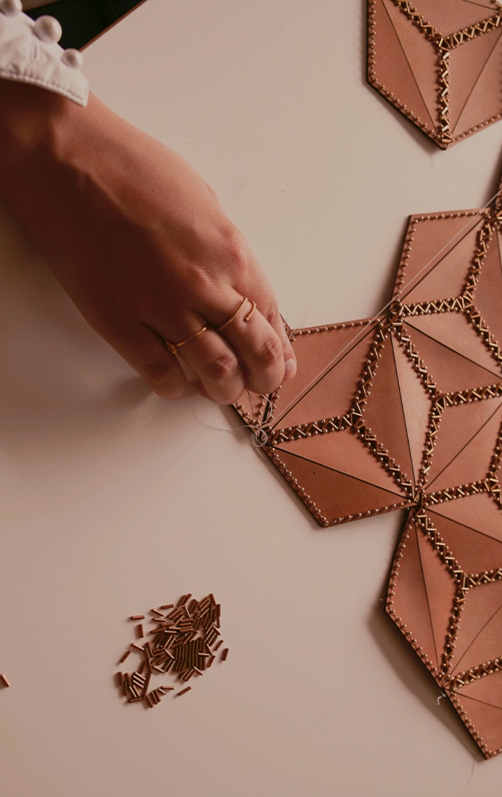 Main assemblant des pièces de cuir géométriques avec des perles