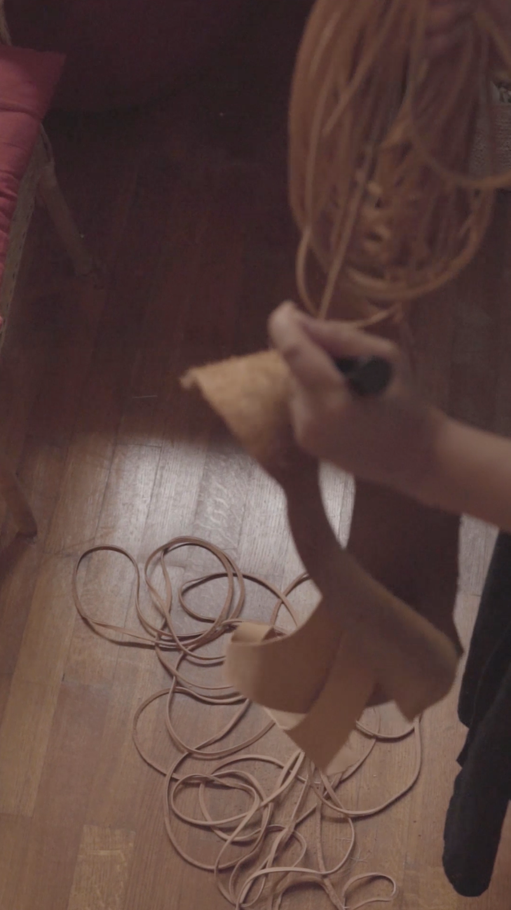 Main découpant délicatement une pièce de cuir, illustrant la valorisation des matériaux nobles.