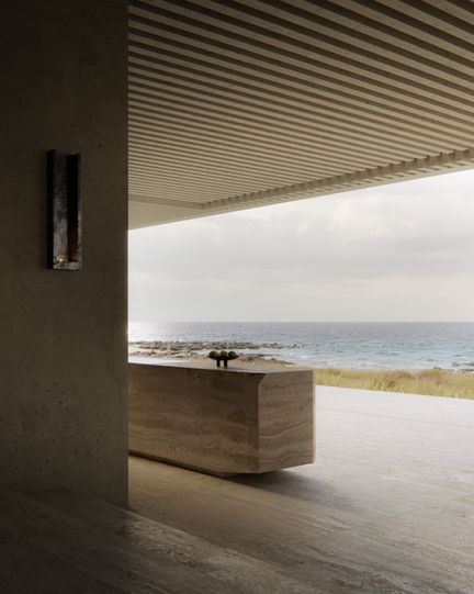 Monolithic stone kitchen island in muted tones, positioned to overlook the ocean through expansive glass openings.