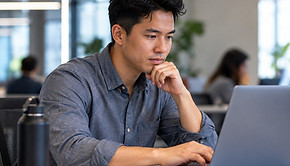A professional working thoughtfully at a laptop in a bright office