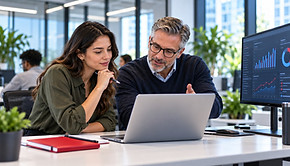 A mentor and a student at a laptop with a data dashboard on the monitor beside them