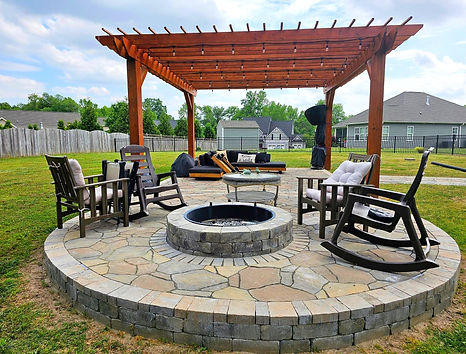 Round paver patio with firepit, chairs, and wooden pergola.