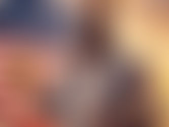 Bearded man with sunglasses holds beer in front of a U.S. flag at sunset, wearing a shirt and suspenders. Relaxed, patriotic mood.