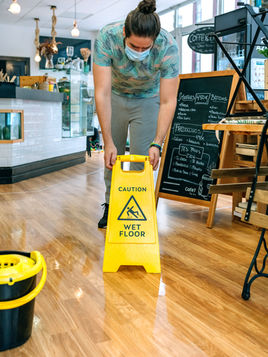 Coffee shop employee placing yellow wet floor sign down on floor.