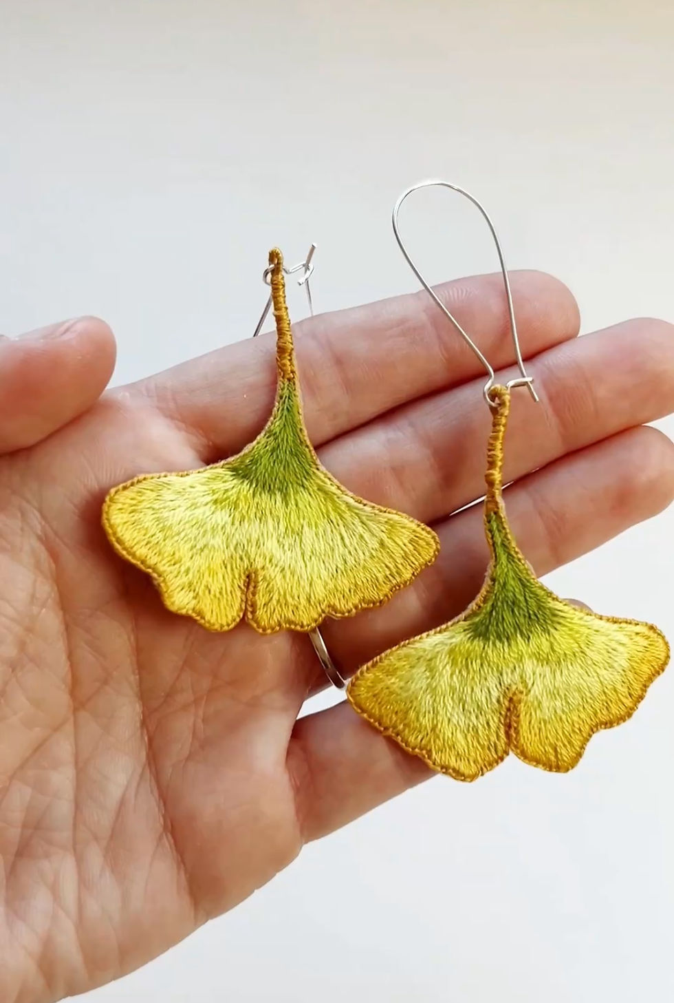 Hand holding two embroidered gingko leaf earrings