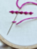 One line of Palestrina knots have been stitched with 5 knots. Below it the Palestrina knot is being formed by sliding the needle downwards underneath the straight stitch.