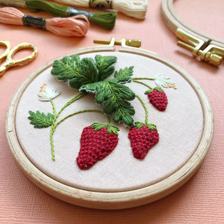 3D stumpwork strawberry embroidery on table with threads, embroidery hoop, and scissors