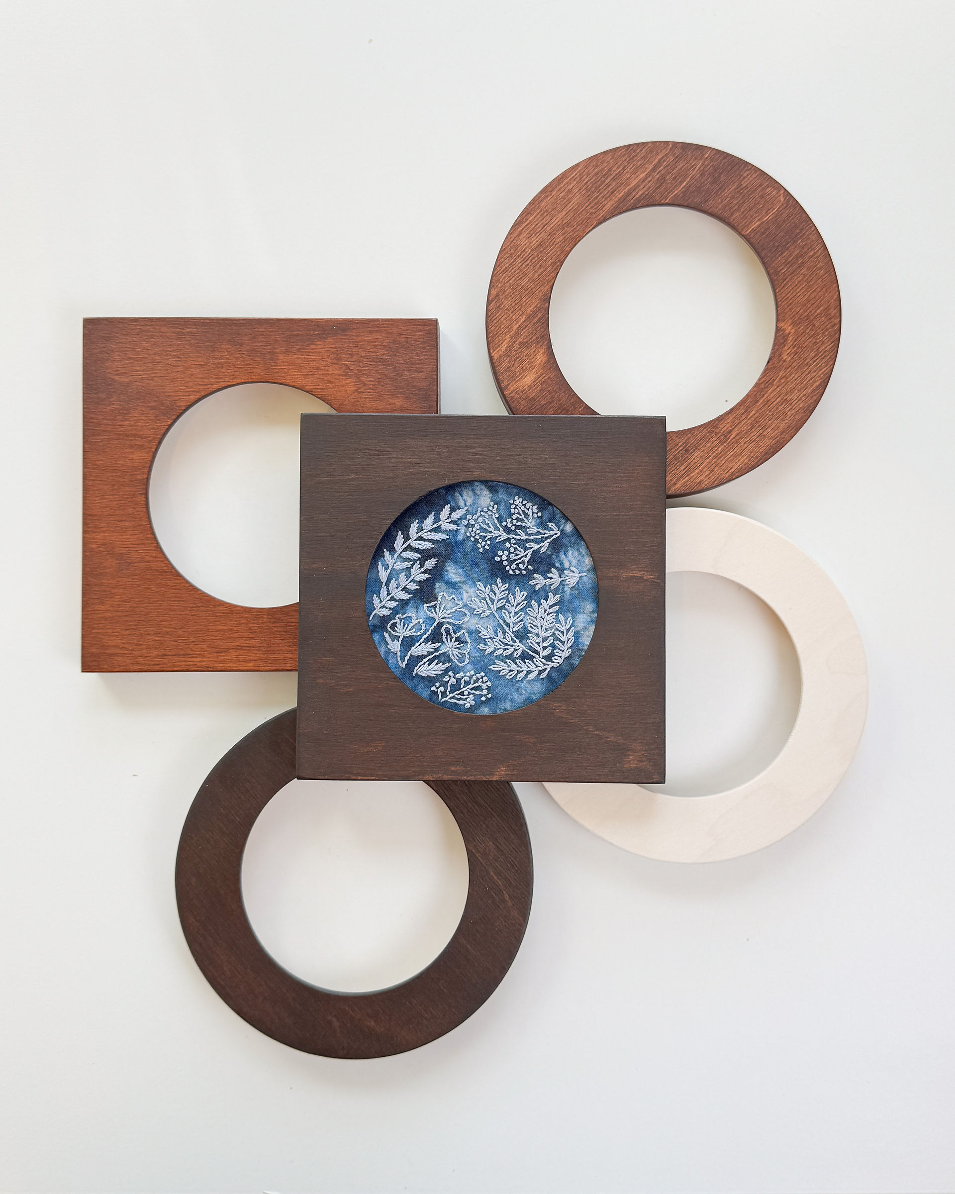 Cyanotype embroidery in square hoop frame on top of other hoop frames