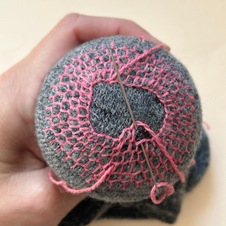 Hand holding a grey sock, embroidered with pink thread in a honeycomb darn pattern
