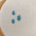 white fabric in an embroidery hoop with three oyster stitches in blue thread