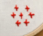 white fabric in an embroidery hoop with 7 four-legged knots stitched in orange thread