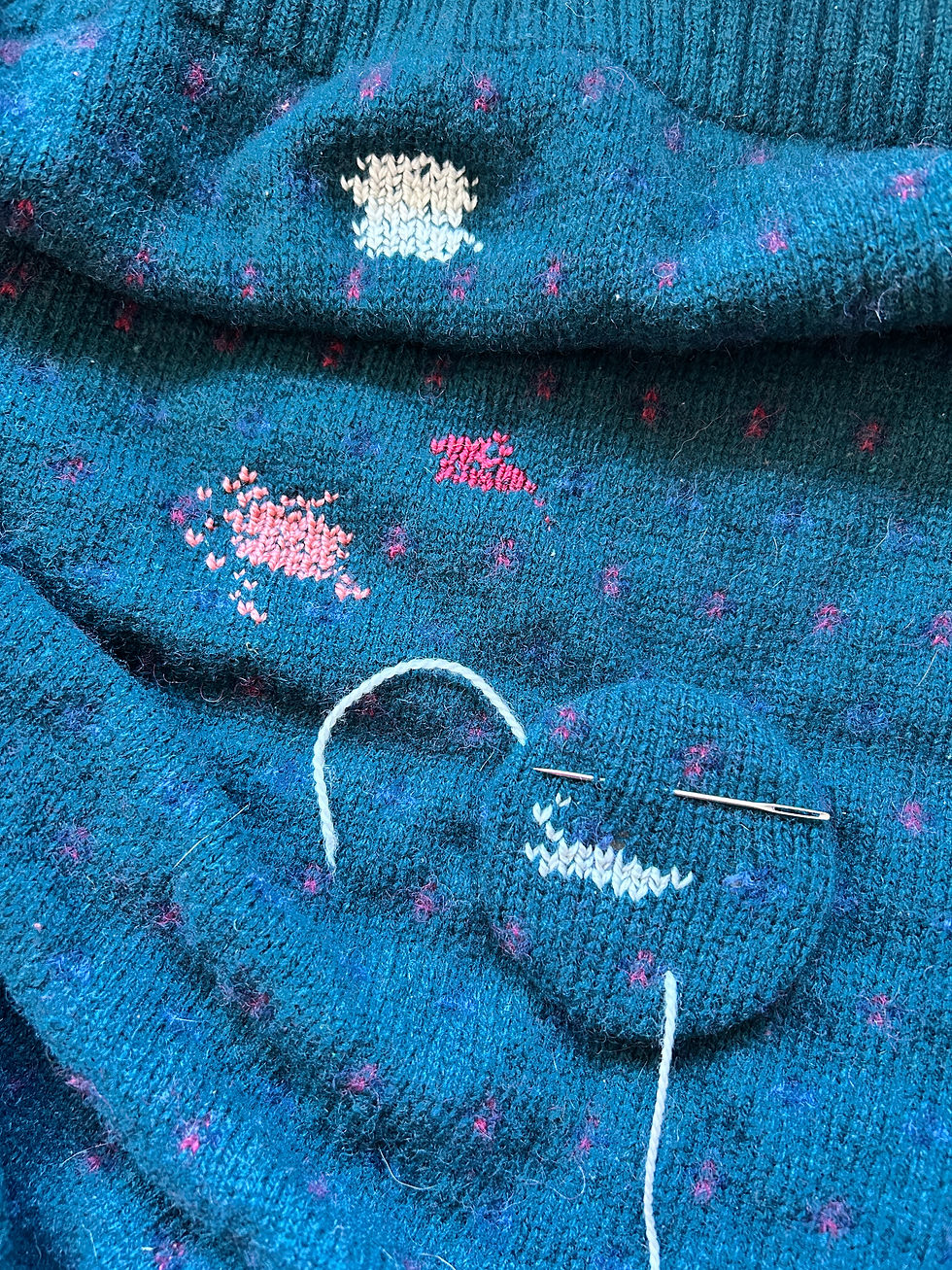 Green wool sweater with patches of cream, pink, and red Swiss darning.