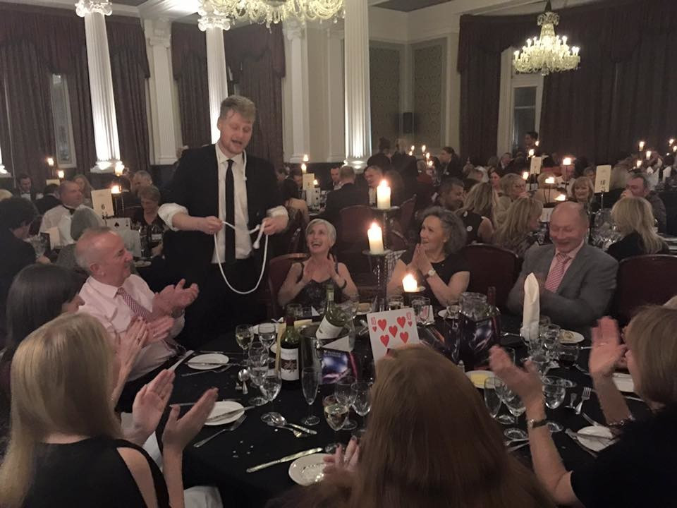 Close-Up illusionist performs some rope illusions for a group around a table at a dinner event