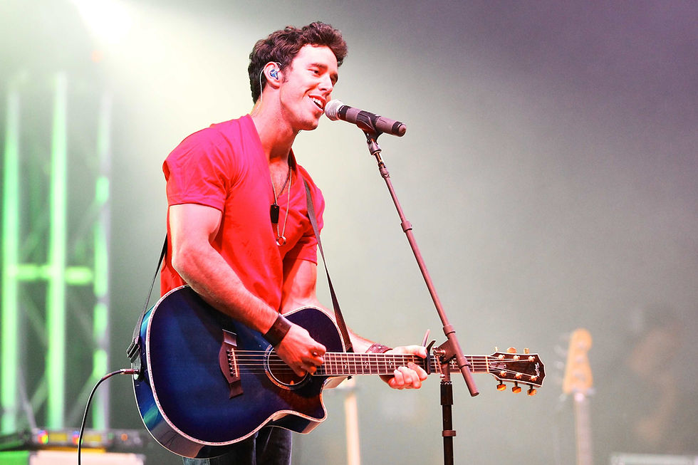 singer in red t-shirt performs and plays a blue acoustic guitar while singing on stage
