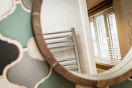 Close up of a circular mirror against mosaic tile backsplash.