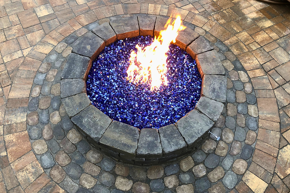 Fire pit with bright flames on blue glass stones, surrounded by circular brick patio. Warm and cozy outdoor ambiance.