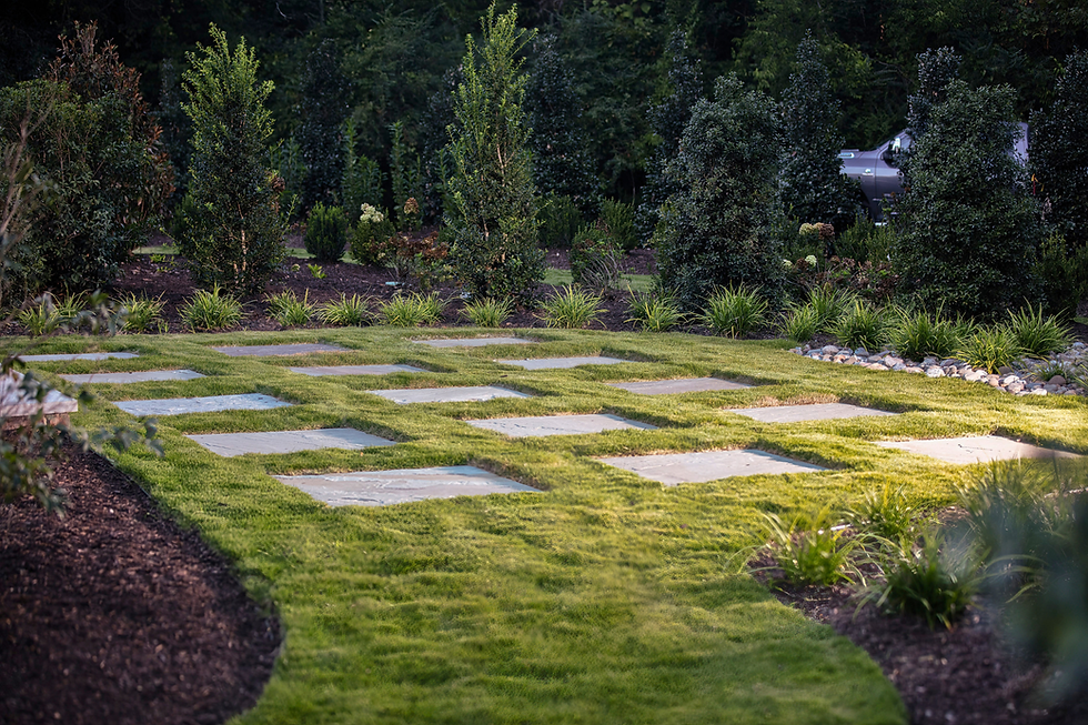 Manicured garden with stepping stones, lush grass, shrubs, and a partially visible truck in the background under soft light.