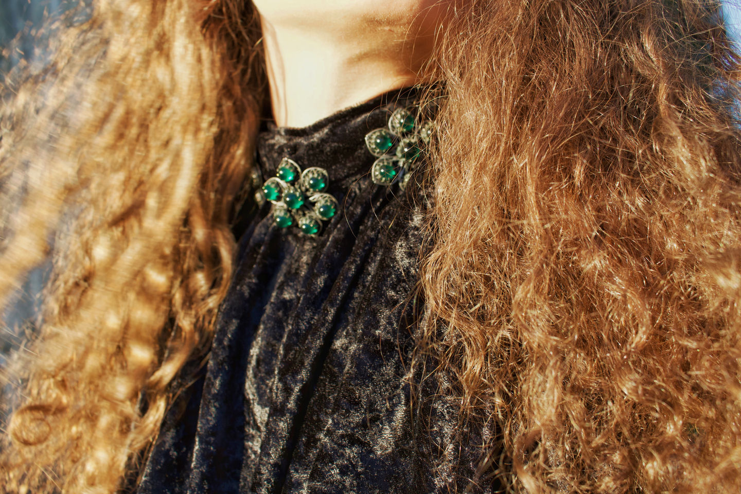 Close up of a woman modeling the Yvonne and Mitchel upcycled velvet button tie halter top, showcasing three antique flower metal buttons on the collar with green stones inside of them.