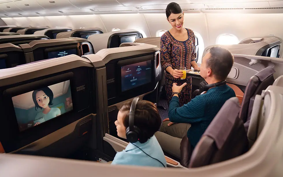 Flight attendant serves juice to a smiling passenger in business class. A child watches a cartoon on the seat screen. Calm, cozy cabin.