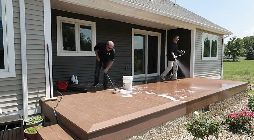 Two people washing a composite deck in sections, one scrubbing and one rinsing with a hose