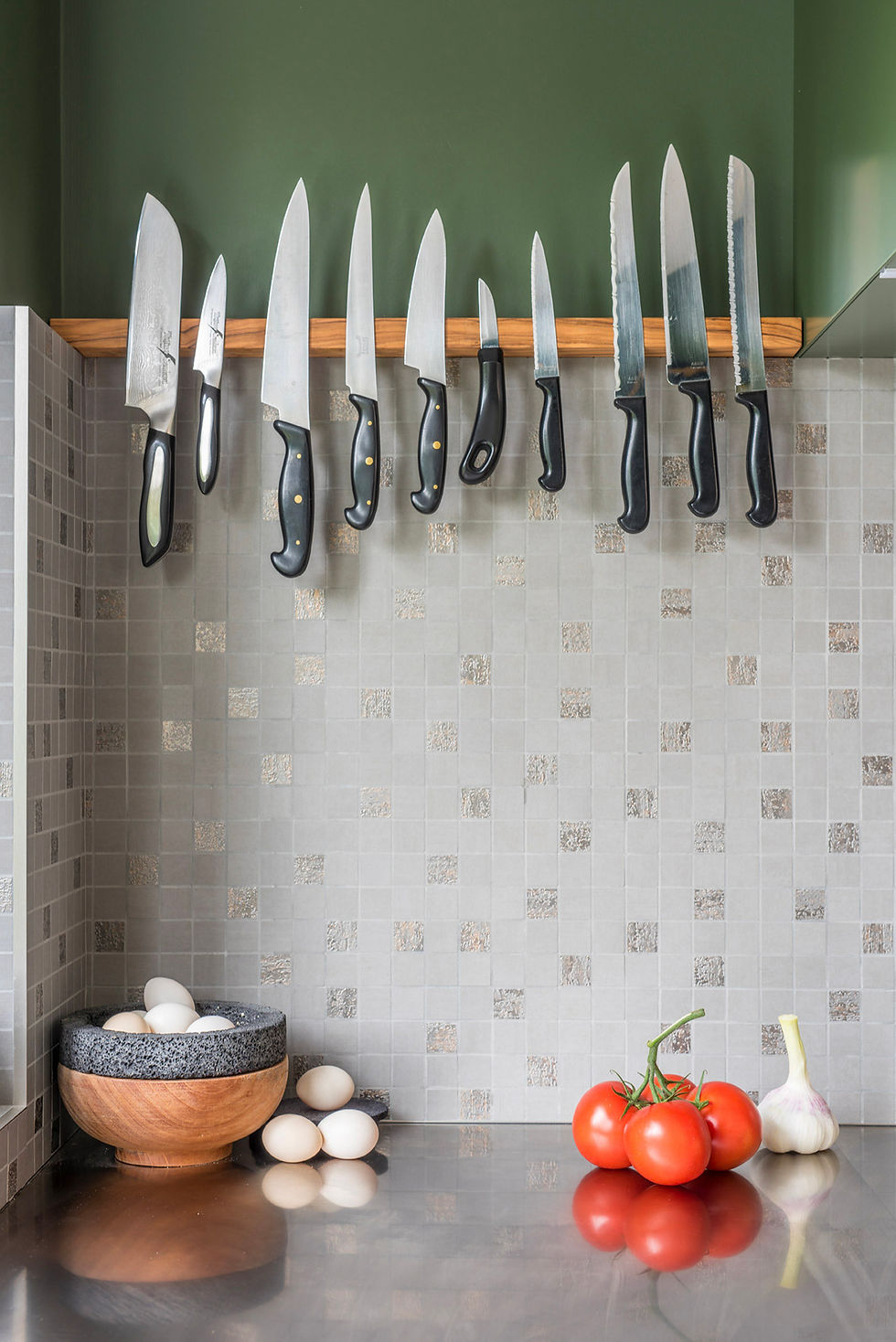 Handmade olivewood magnetic knife holder beneath dark green kitchen cabinetry