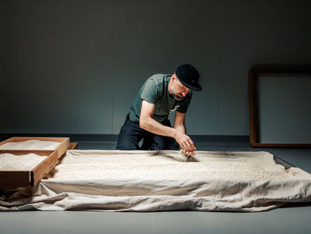 Hamish sifts rice in a dim room, working over a cloth-covered tray beside wooden frames.