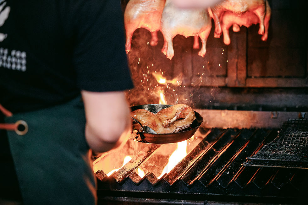 A chef grills a pan with chicken over an open flame.