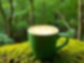 a flat white coffee in a green cup with latte art in front of a lush green forest on a mos