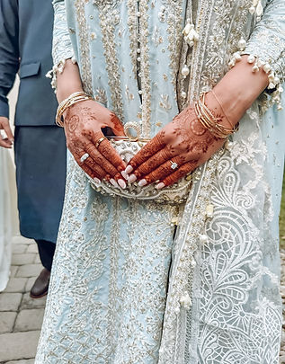 Close-up of a bride in a soft blue embroidered traditional outfit holding a jeweled clutch, showcasing elegant bridal henna