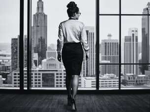 Curvy red-haired woman in office attire walking toward desk with Melbourne skyline view