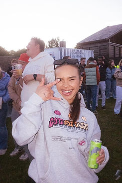 Jente som holder en grønn energi drikk, i grå hettegenser mens hun gjør rocke tegntet med hånda