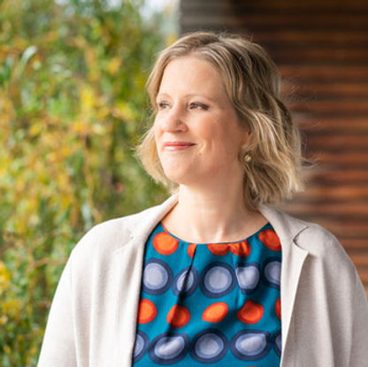 Lächelnde Frau (Michaela Hatz) mit blondem, schulterlangem Haar, die seitlich blickt und in der Natur steht