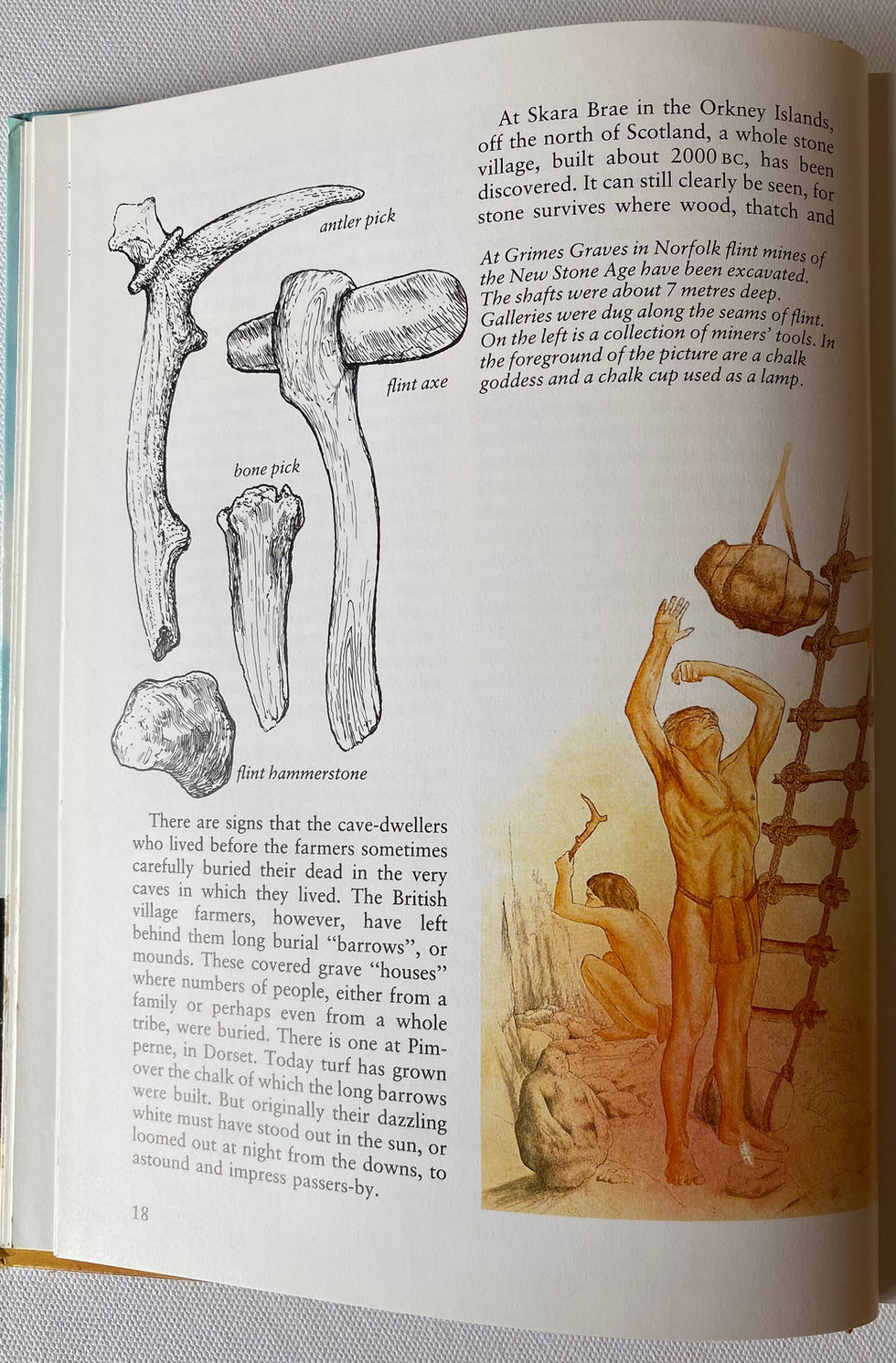 Open book, non-fiction, A Children's History of Britain and Ireland. A figure hammering flint, in a flint mine, another figure is overseeing a bag of flint being raised, Grimes Graves in Norfolk. Flint mines of The New Stone Age. Chalk goddess and chalk lamp are in the foreground. Illustration by David Salariya