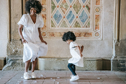 Une femme cheveux afro et robe blanche dans avec sa fille du même style dans un cadre romanesque