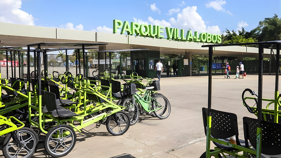 Fotografia da entrada do Parque Villa-Lobos no bairro do Alto de Pinheiros, mostrando fileiras de quadriciclos de aluguel verdes no primeiro plano. O letreiro principal diz 'PARQUE VILLA-LOBOS'. Pessoas caminham pela praça sob um céu ensolarado. Esta imagem captura uma das principais atrações e coisas o que fazer no Parque Villa-Lobos para um roteiro no Alto de Pinheiros.