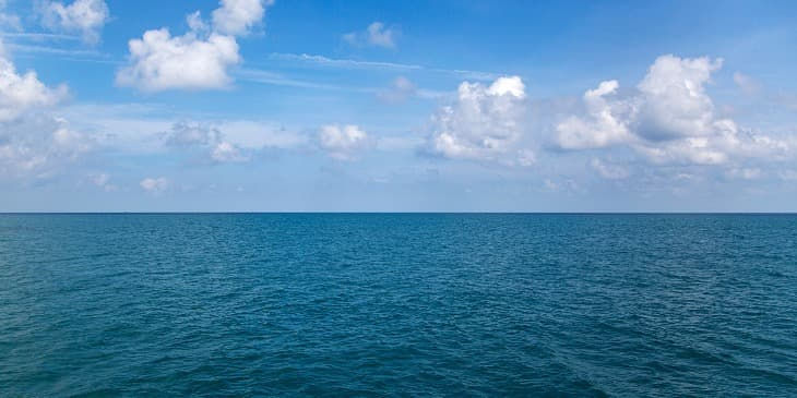 O mar azul bem calmo e um céu cheio de nuvens brancas
