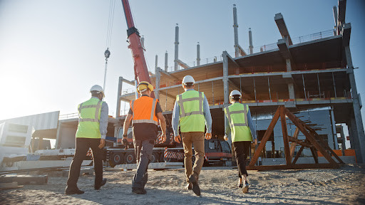 a group of four construction workers walks across a building site.