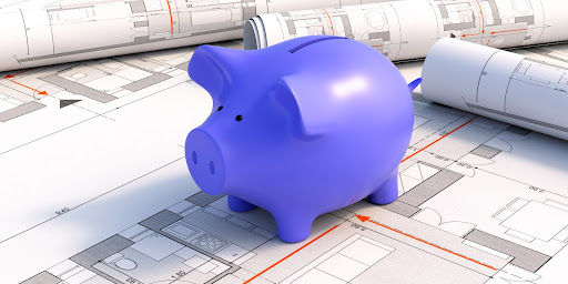 A piggy bank sits on some building plans. Will you be able to afford the cost of your construction project?