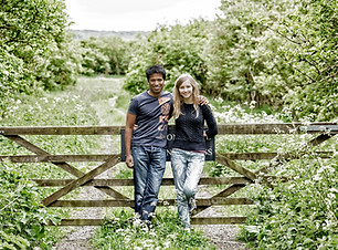 Engagement couple leaning on a five bar gate in a filed.