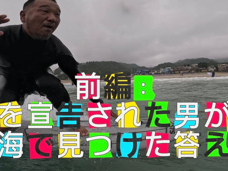 ウェットスーツで波に乗る奥村哲次のクローズアップ。画面に「前編:死を宣告された男が、海で見つけた答え」のタイトル文字。背景は福島・豊間海岸の海と町並み。