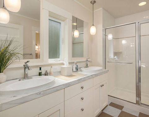 Elegant bathroom with white double-sink vanity, pendant lighting, and a clean modern look, exemplifying contemporary residential construction.