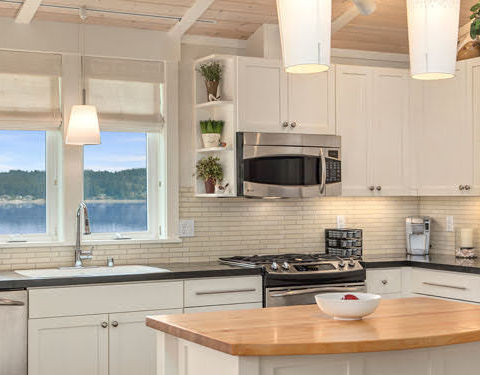 White and gray kitchen with lake views through wide windows, illustrating custom luxury home builders’ attention to scenic living.