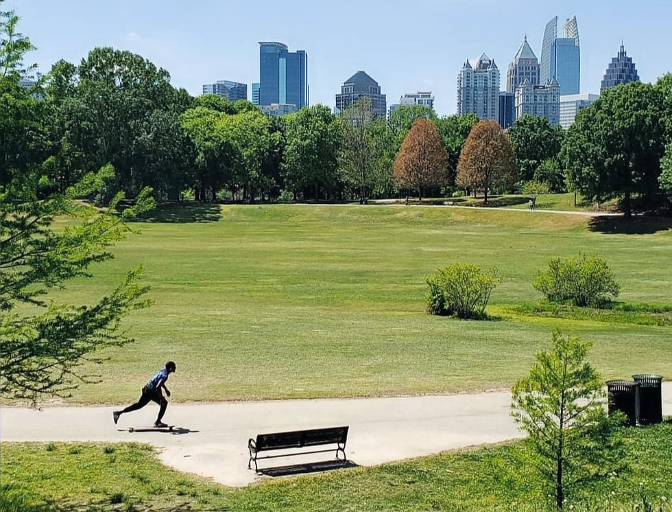 A guy on a skateboard at Piedmont Park with the Atlanta skyline in the distance
