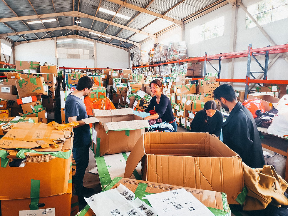 4 volunteers are in a warehouse sorting through cardboard boxes and smiling at each other.